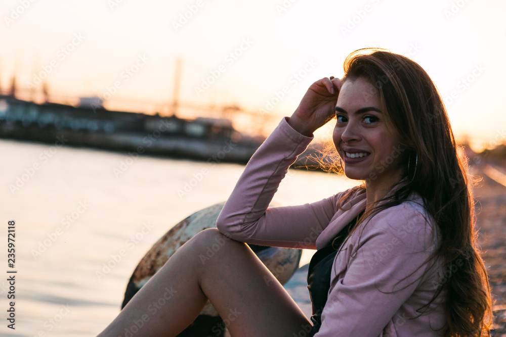 Charming young woman in casual wear sitting near water with boat Charming young woman in casual wear sitting near water with boat