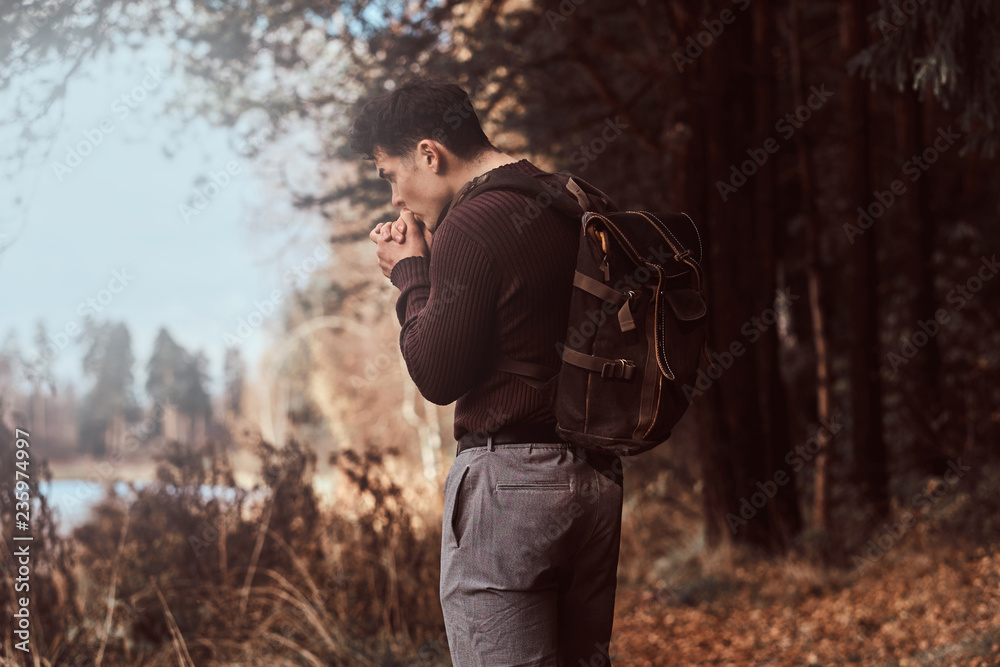 A young hiker wearing sweater warms hands in the cold autumn forest.