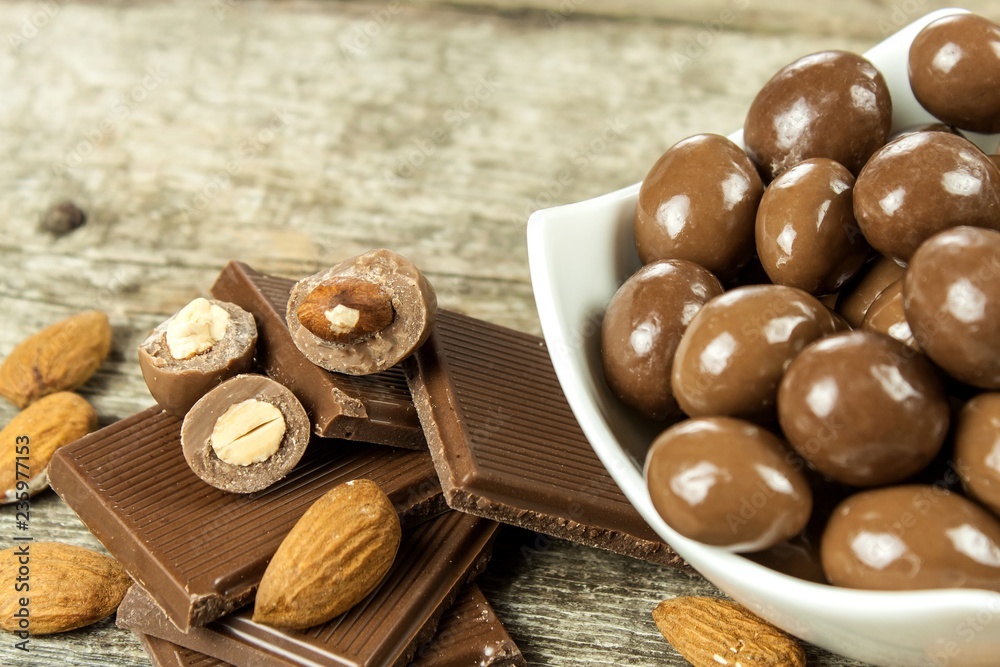 Almonds in chocolate glaze on a old wooden table. Unhealthy food. Risk