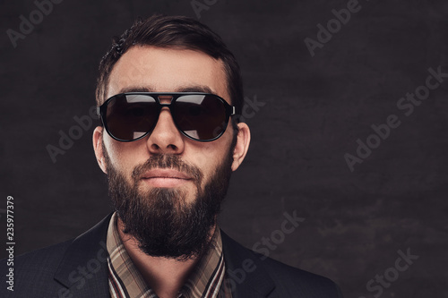 Close-up portrait of a bearded man wearing a suit and sunglasses.