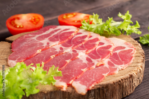 Gorgeous delicious slicing of jamon on a natural wooden plateau with green lettuce and tomatoes. Luxury elite premium snack.
