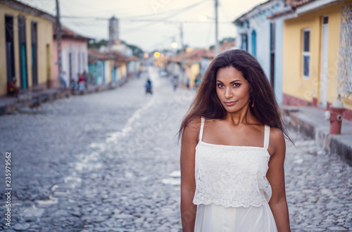 Beautiful dark skinned young lady in white dress standing in the old streets of Trinidad in Cuba.
