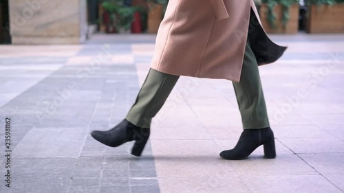 Legs of woman in black boots walking in the street