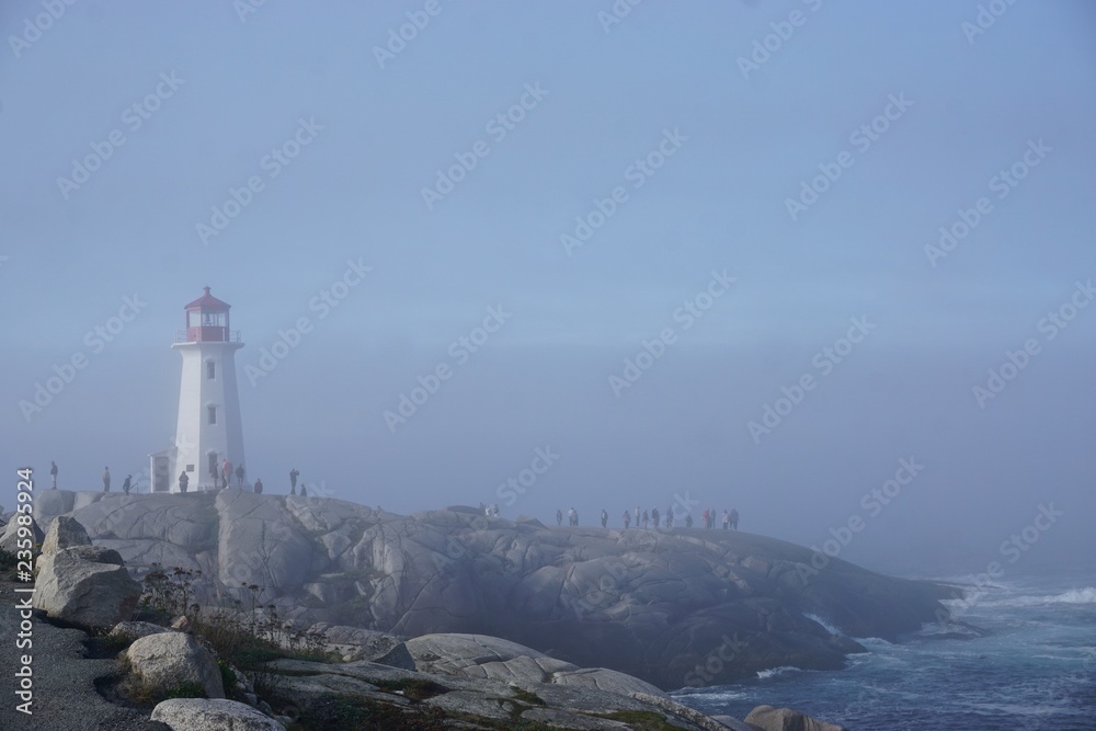 Peggy’s Cove, Nova Scotia, Canada: Peggy’s Point Lighthouse (1914) shrouded in morning mist with waves breaking on a rocky coast.
