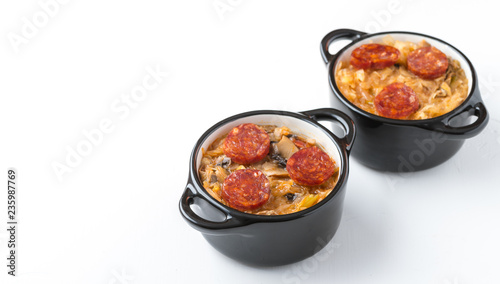 Slovak Christmas national cabbage soup in two small black pots with sausage on the white background.