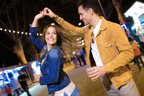 Carefree young couple dancing holding hands in eat market in the street at night.