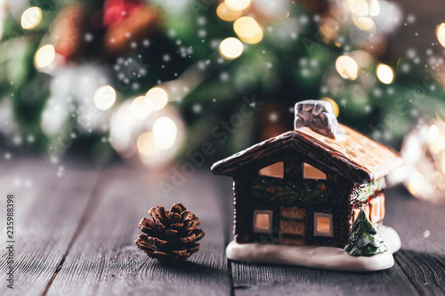 Christmas village house with candle inside on rustic table with christmas tree in the background, bokeh lights, snow and smoke effect, copy space