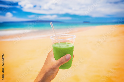 Green smoothie juice detox drink selfie man holding plastic cup on beach summer background. Food picture of healthy nutrition diet in outdoor lifestyle.
