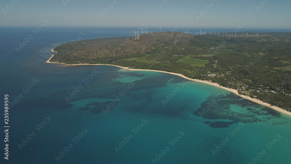 Aerial view of beautiful tropical beach Saud with turquoise water in blue lagoon, windmills. Pagudpud, Philippines. Ocean coastline with sandy beach and palm trees. Tropical landscape in Asia.