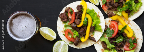 Tasty tacos with beef and vegetables, beer and lime on a black surface, overhead view. Mexican kitchen. Flat lay, top view, from above. photo