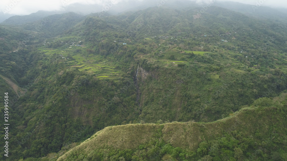 Aerial view of rice fields and agricultural land on the slopes of the mountains. Mountains covered forest, trees, waterfall. Cordillera region. Luzon, Philippines.