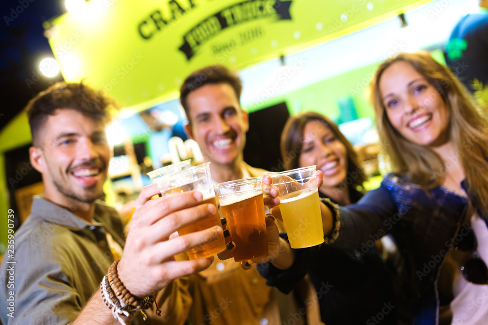 Attractive young friends looking at camera while toasting with beer in eat market in the street. Attractive young friends looking at camera while toasting with beer in eat market in the street.