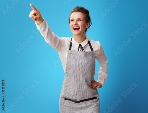 smiling young scrubwoman in apron on blue pointing at something photo