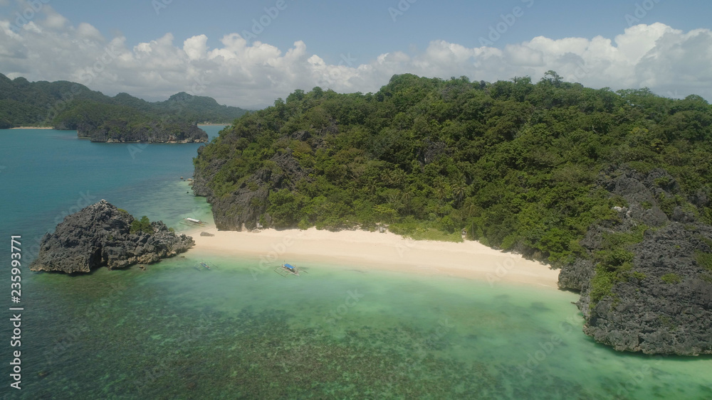 Aerial view Matukad island with sand beach and turquoise water in blue lagoon among coral reefs, Caramoan Islands, Philippines. Landscape with sea, tropical beach.