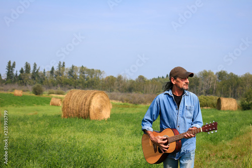 Fotografija Handsome man playing a and acoustic guitar in the field