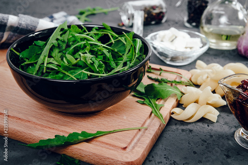 Arugula in a black, large bowl. Green, fresh arugula in a bowl on a wooden stand and a stone counter. The concept of preparing a fresh and healthy salad. Healthy nutrition, taking care of health.