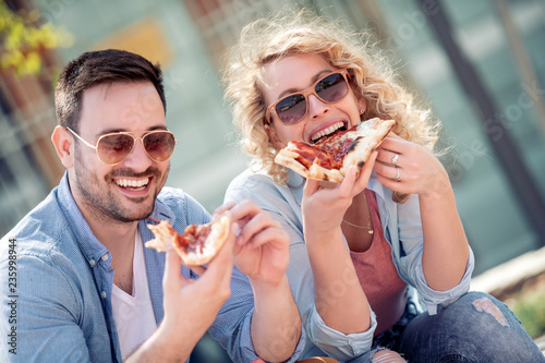 Couple eating pizza snack outdoors.