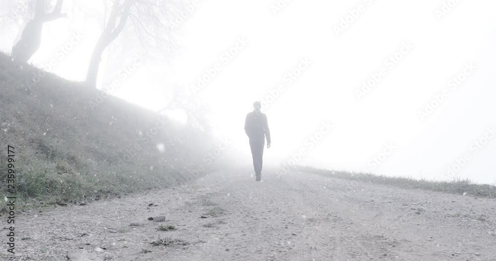 Man walks alone on foggy winter season countryside road durnig snowfall. 