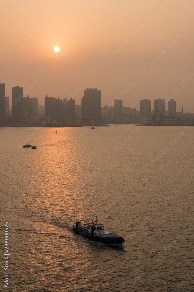 Fototapeta premium Sun rising behind the tall city skyline of Qingdao in China