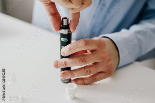 The man unscrews the e-cigarette to fill up the liquid, clean the cigarette. The concept of using e-cigarette, vaping. Addiction to nicotine, topping up liquid. Problems with addiction. photo