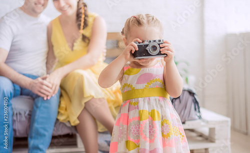 Little cute girl with a camera. Happy parents in the background