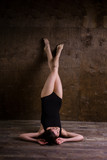 Theme is a sport and a beautiful sexy woman. Young caucasian girl lying on the floor kicking up posing in a black sports swimsuit clothes with bare feet on a dark wooden background in the studio