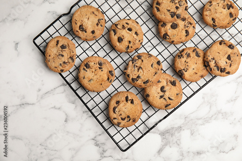 Cooling rack with chocolate chip cookies on marble background, top view