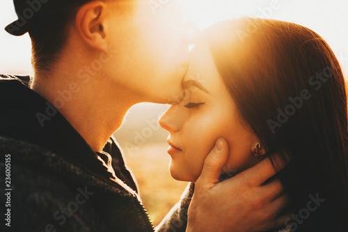Side view of crop male kissing pretty girlfriend in forehead while spending time in nature on sunny day.Crop guy kissing girlfriend in forehead in nature photo