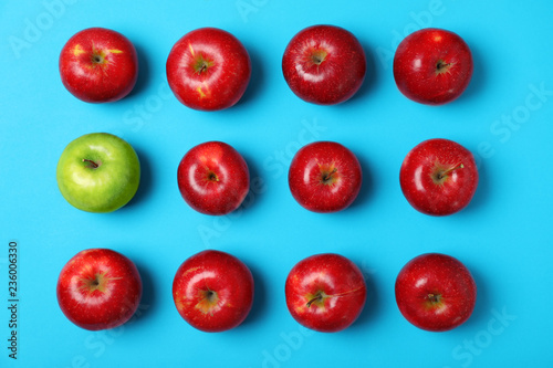 Green apple among red ones on color background, top view. Be different