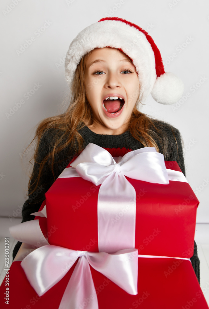 Smiling little girl kid in x-mas santa helper hat with red gift boxes happy smiling shouting yelling Smiling little girl kid in x-mas santa helper hat with red gift boxes happy smiling shouting yelling