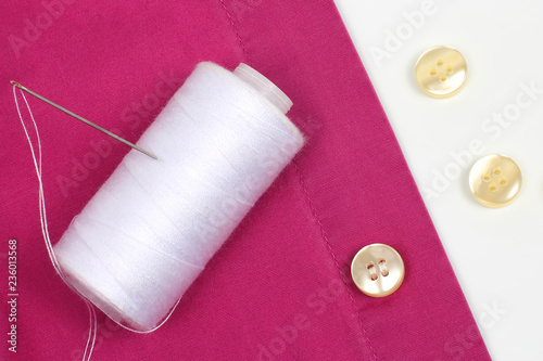 Coil with white threads and a needle and sewn pearl buttons on the shirt