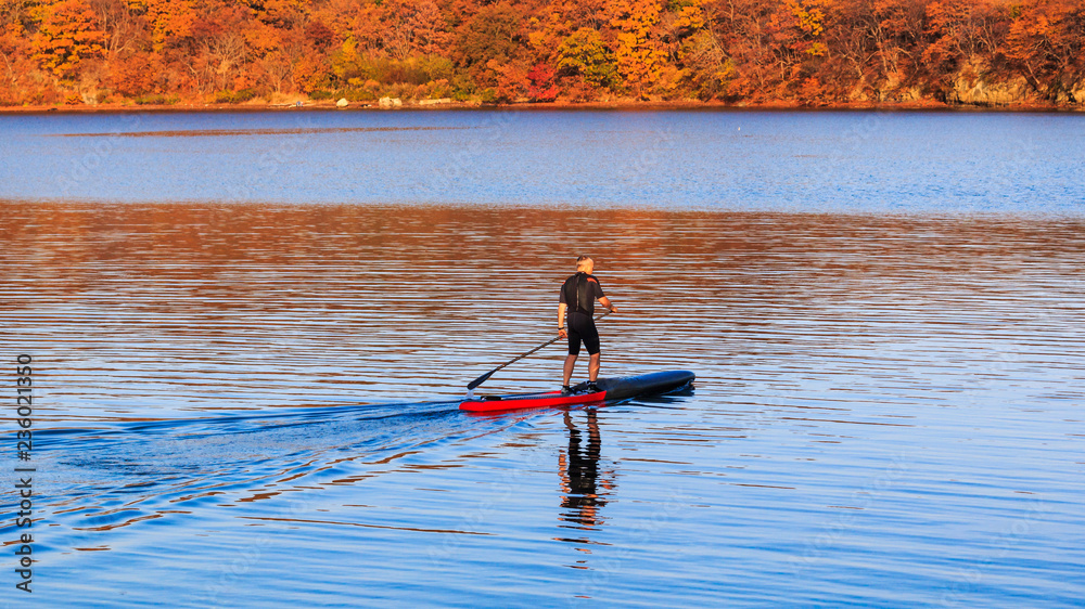 An elderly man rides in the calm sea on an inflatable sup board