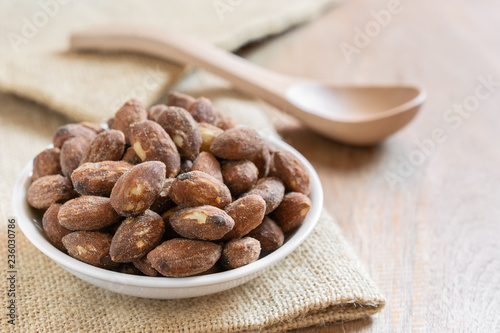 close up of salt roasted almond in a small ceramic dish on wooden table. healthy snack concept.