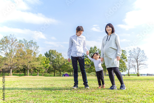 青空の公園で手を繋ぎ散歩をする家族。家族,妊娠,親子,愛,幸せイメージ © chikala