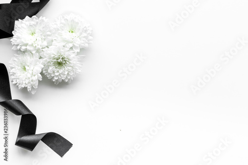 Funeral symbols. White flower near black ribbon on white background top view space for text