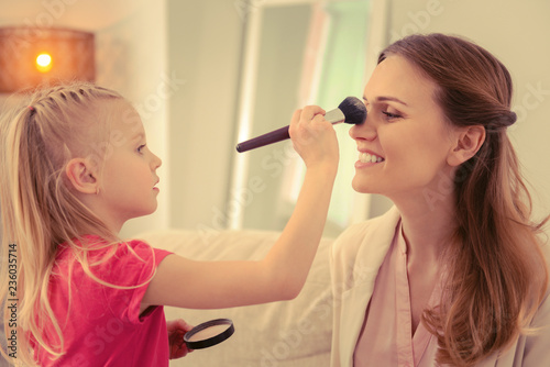 Cheerful cute girl applying facial powder on her moms face