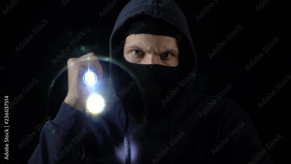 Lawbreaker in balaclava mask flashing torch, searching for important information Lawbreaker in balaclava mask flashing torch, searching for important information
