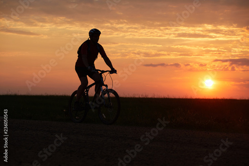 Silhouette of a cyclist on the background of the sunset. Biker rides on the road in the evening. Red-yellow background outdoors