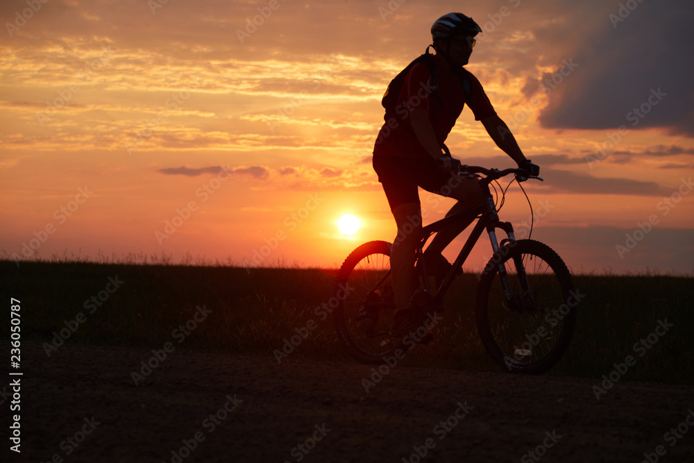 Silhouette of a cyclist on the background of the sunset. Biker rides on the road in the evening. Red-yellow background outdoors Silhouette of a cyclist on the background of the sunset. Biker rides on the road in the evening. Red-yellow background outdoors