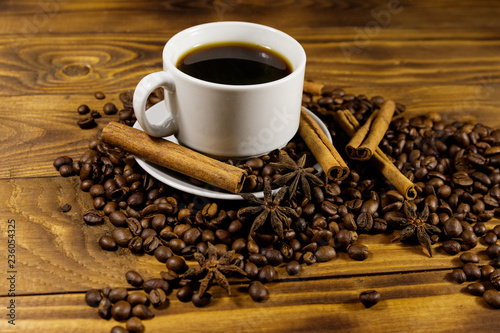 Cup of coffee, roasted coffee beans, star anise and cinnamon sticks on wooden table