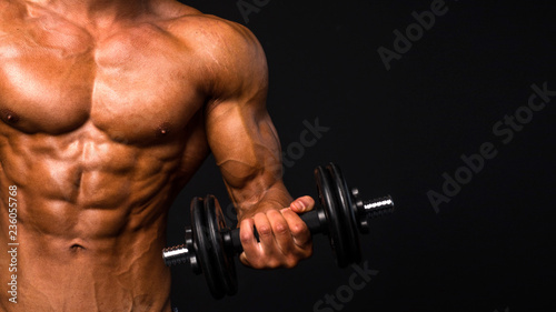 fit male torso with dombbell on dark background. Perfect abs, bicep, chest.