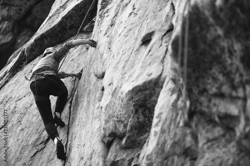 A girl climber climbs up a vertically rocky wall. Competitions in sport climbing. Black and white.