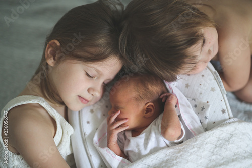 sisters care hug newborn, baby sleeping in cocoon