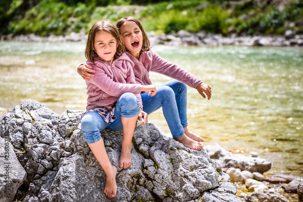 Identical twin girls sitting on river rock after nature hiking.