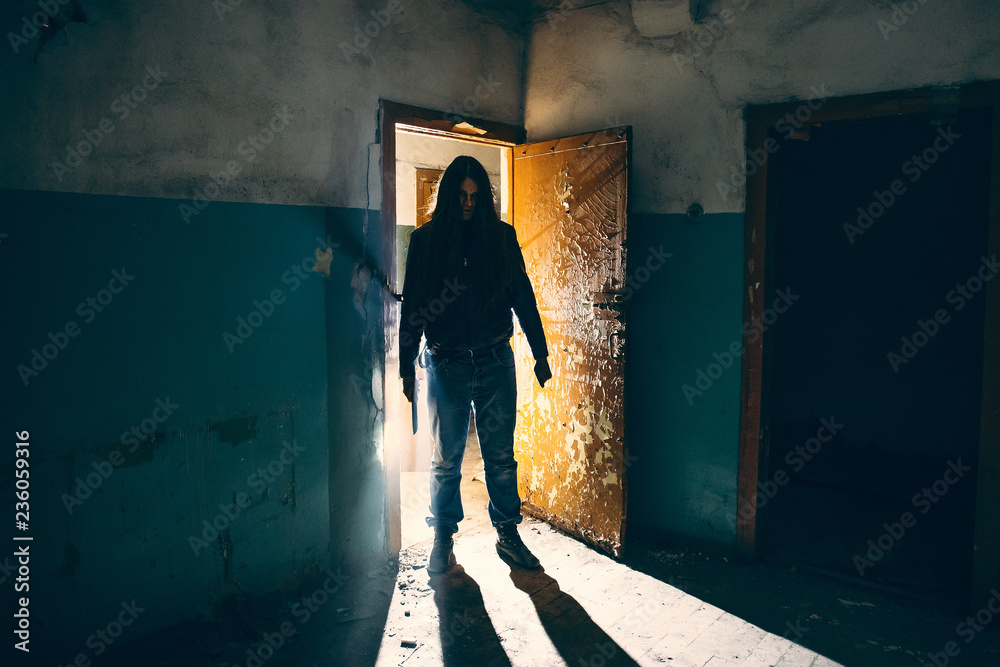 Silhouette of criminal or maniac with knife in hand in old scary building, serial killer with cold weapon