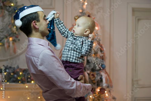 Father and son on New Year's Eve. Baby on the hands of dad in Santa Claus hats