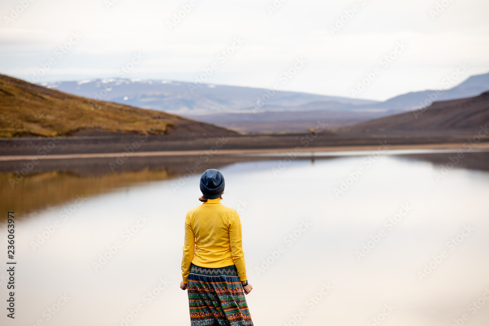 The girl in yellow admires the view of the river and the hill in the rays of the rising sun. Early morning day in Iceland. Car tourism in Iceland.