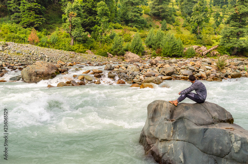 A person sitting on a rock in front of a river in Lidder Valley, at Pahalgam in Kashmir photo