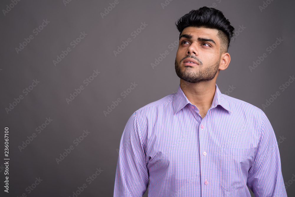 Obraz premium Young handsome Indian businessman against gray background