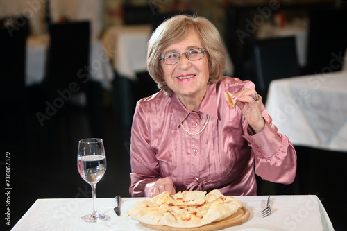 An elderly woman with glasses eating in a restaurant bread cake. The concept of a decent old age. Pensioners on vacation. Photo in interior.